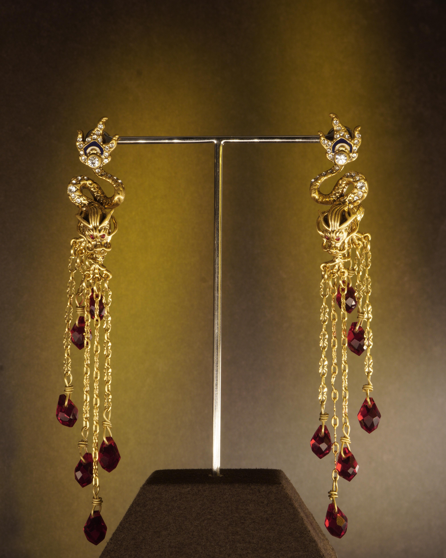 Real studio photograph of the MAGNAURA Crowned Dragon drop earrings under warm light and shadow