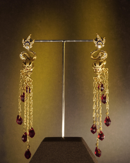 Real studio photograph of the MAGNAURA Crowned Dragon drop earrings under warm light and shadow
