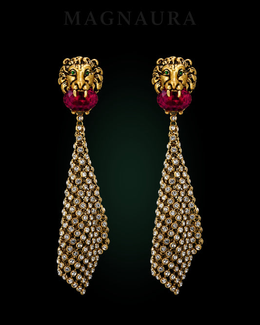 Pair of MAGNAURA Gilded Lion drop earrings with green eyes, crimson centres and clear tassels against a deep green-black chamber